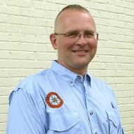 Erik Kulick leaning aginst wall with True North badge on blue shirt